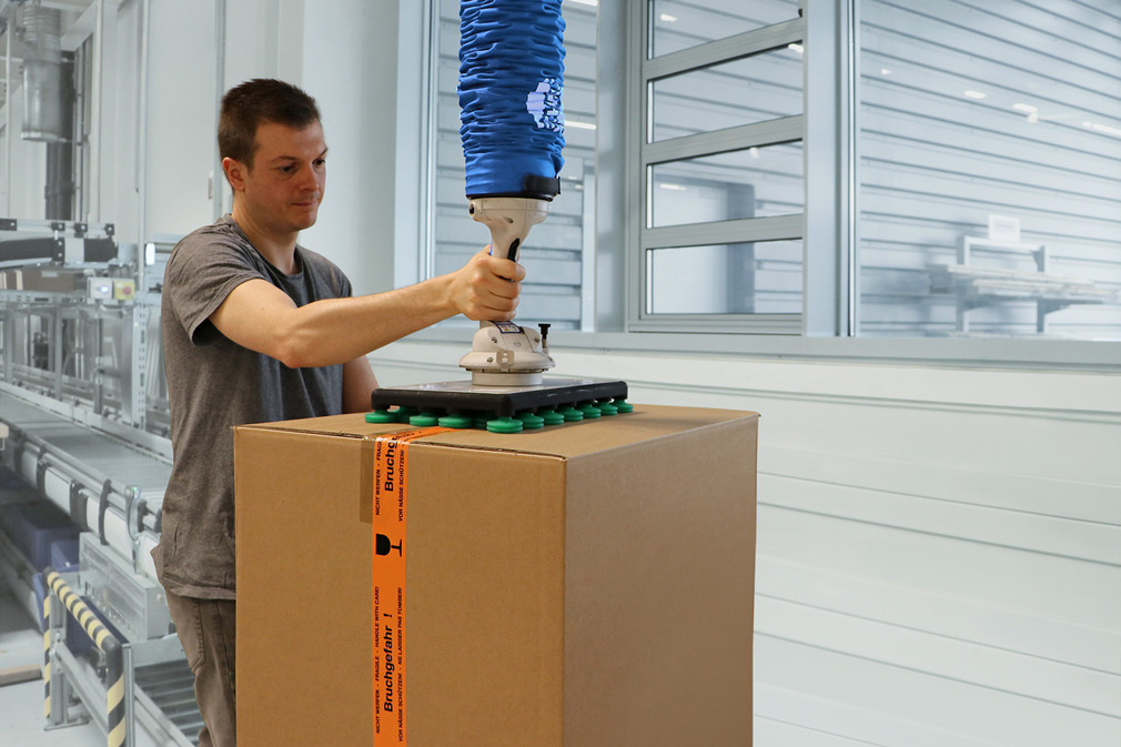 The vacuum tube lifter JumboFlex makes it easy to pick up and move heavy cardboard boxes.