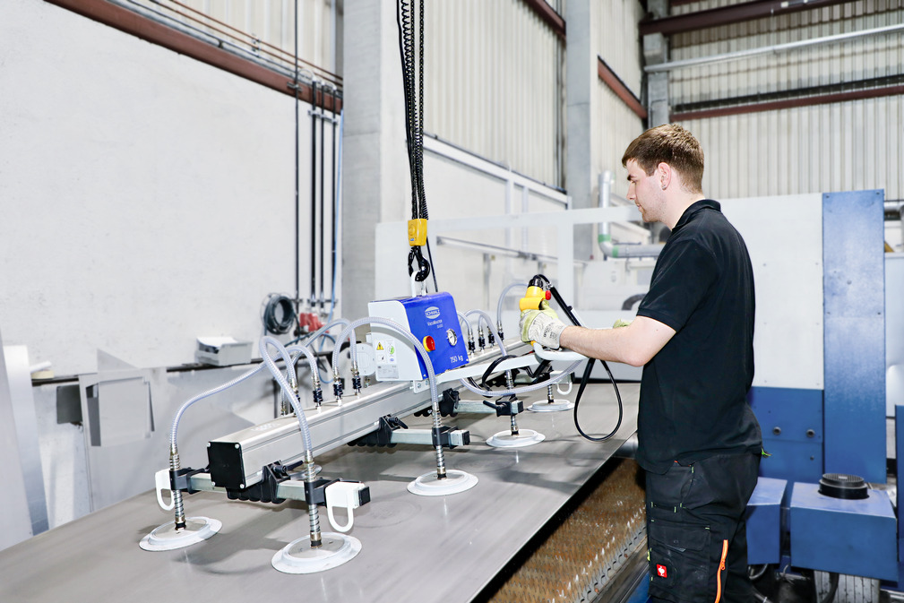 Der Mitarbeiter legt die Großformattafel mit Hilfe des Vakuum-Hebegerätes VacuMaster auf die Zuführeinheit der Laserschneidanlage.